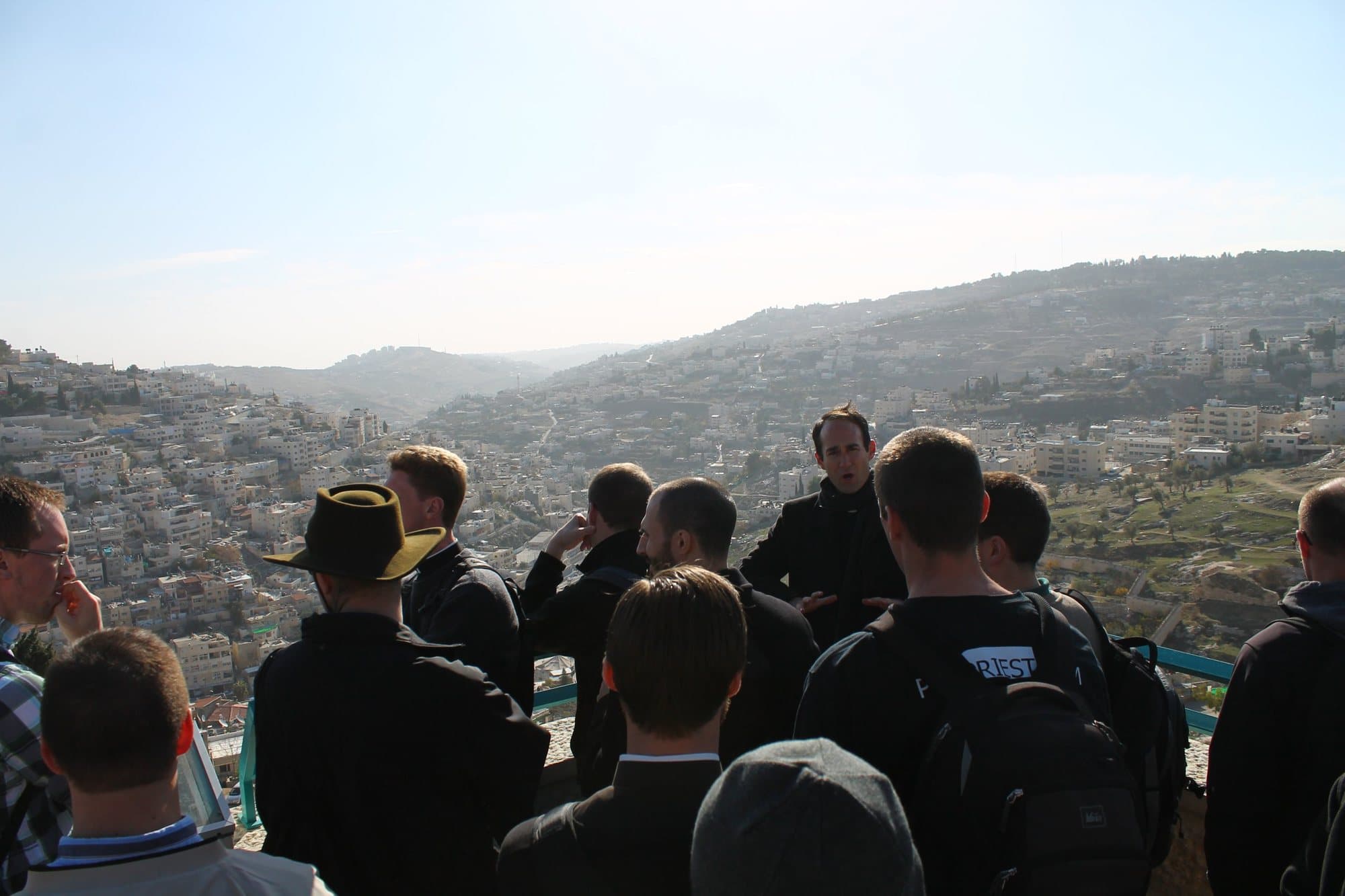 James Platania speaking to a group of seminarians gathered at a hillside overlook in Jerusalem, with the city spread across the valley and slopes behind them.
